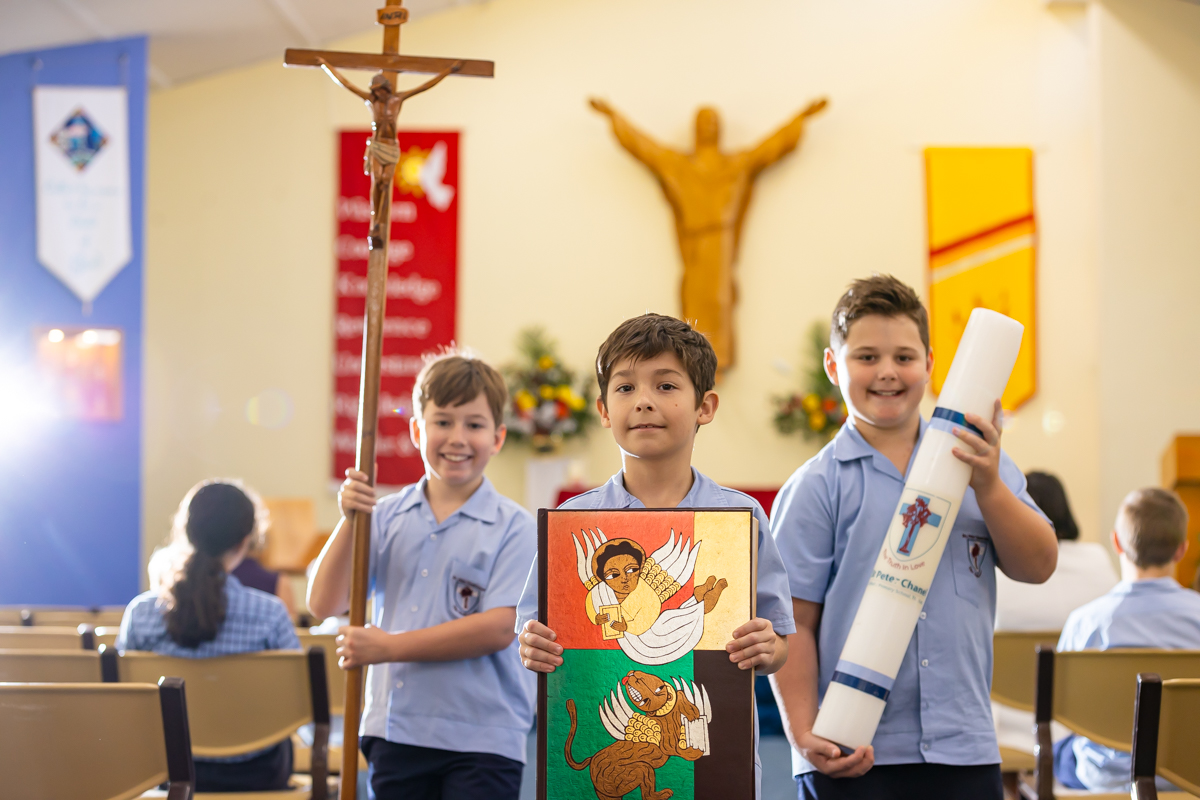 Students standing at the front of a church holding faith symbols, highlighting Catholic identity, shared worship and active participation in religious life within the school community