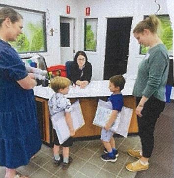 Students sharing learning work with educators at the school reception area, highlighting confidence, communication and supportive interactions within the school community