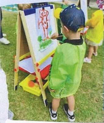 Child painting at an easel outdoors, highlighting creative expression, fine motor development and learning through art