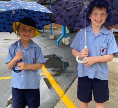 Students holding umbrellas on a wet school day, highlighting care and resilience