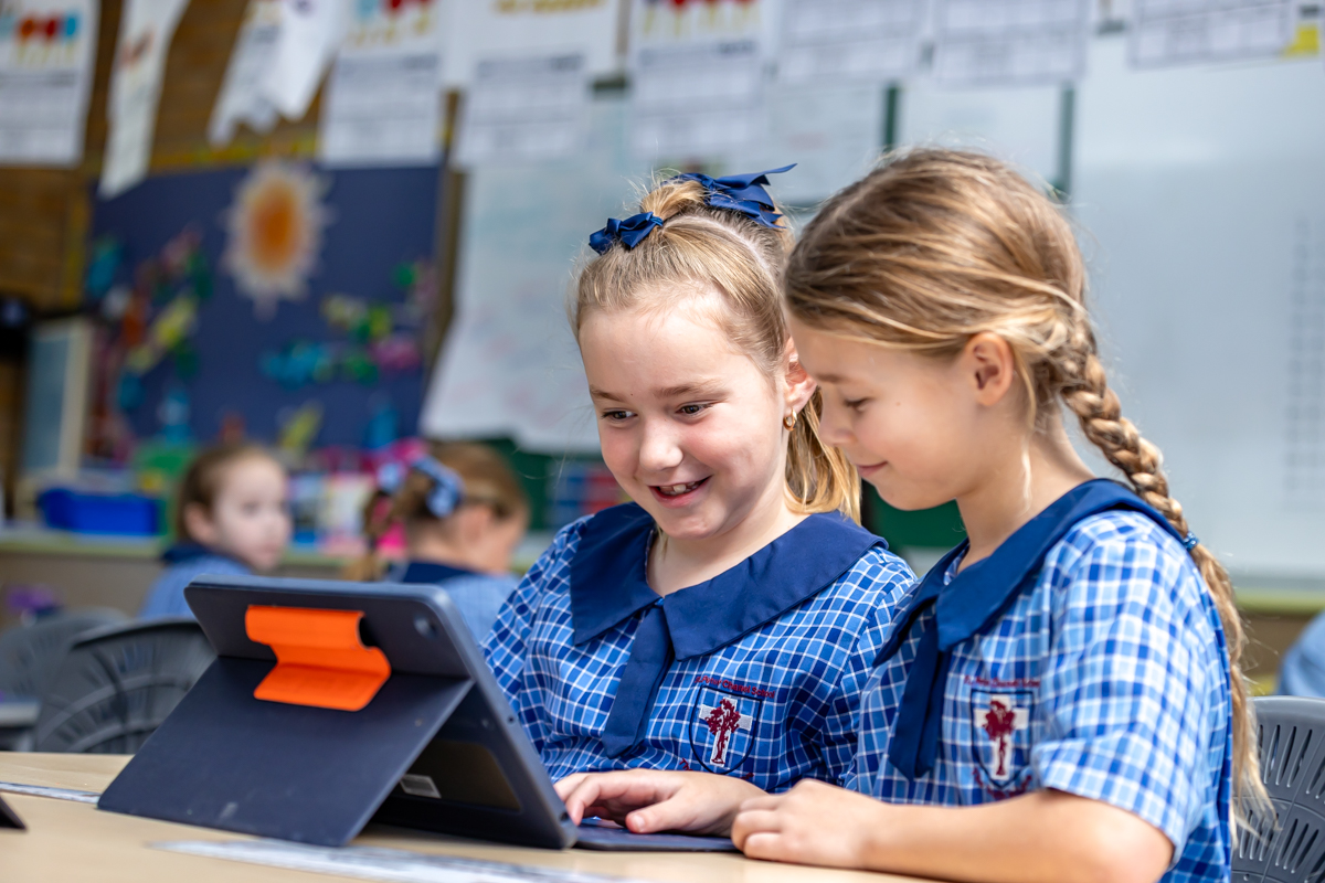 Students collaborating using a tablet in the classroom, highlighting digital learning, peer support and engagement within a primary school learning environment