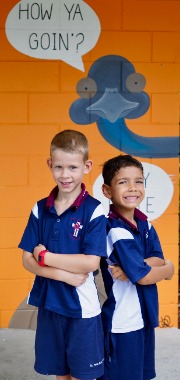 Two students standing confidently in front of a school values mural, highlighting belonging and wellbeing