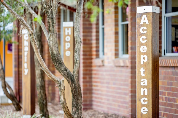 Values pillars displaying Acceptance, Hope and Charity outside the school building, highlighting faith‑based values and character formation within the school community