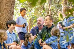Students gathered with two educators outdoors under a tree, highlighting curiosity, shared learning and connection with nature within a supportive primary school environment